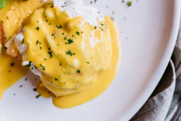 Sluit omhoog Ei Benedictus gediend met salade in witte plaat op houten lijst.