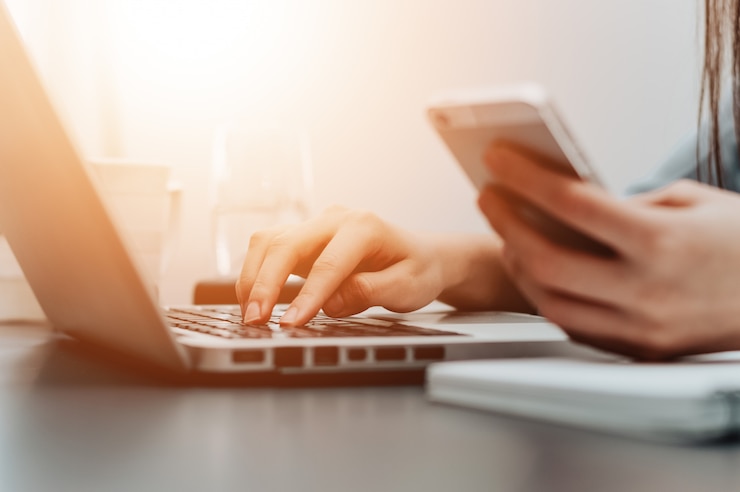 Foto sluit omhoog foto van vrouw gebruikend telefoon en laptop tezelfdertijd.