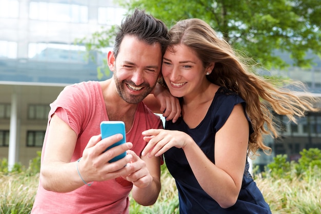 Sluit omhoog gelukkige jonge paarzitting samen met mobiele telefoon