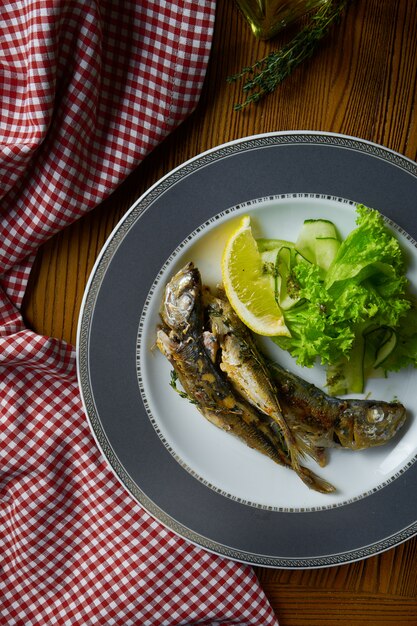 Sluit omhoog Geroosterde vissensprot met salade op witte plaat in samenstelling met rode doek op houten lijst.