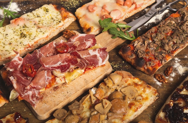 Sluit omhoog geschoten van verscheidenheid van eigengemaakte pizzaplakken. Rechthoekige porties. Italiaans eten. Assortiment zelfgemaakte pizza's.