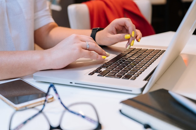 Sluit omhoog handen bedrijfsvrouwenzitting in bureau die en op haar laptop toetsenbordcomputer coworking typen.