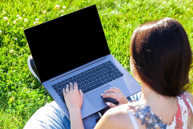 Sluit omhoog handen op toetsenbord. vrouw die op laptop pc-computer werkt met een leeg zwart leeg scherm om ruimte in het park op groen graszonnegras buitenshuis te kopiëren.