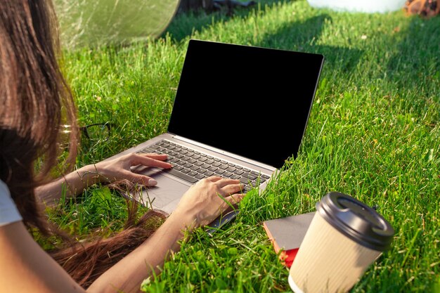 Sluit omhoog handen op toetsenbord. Vrouw die op laptop pc-computer werkt met een leeg zwart leeg scherm om ruimte in het park op groen graszonnegras buitenshuis te kopiëren.