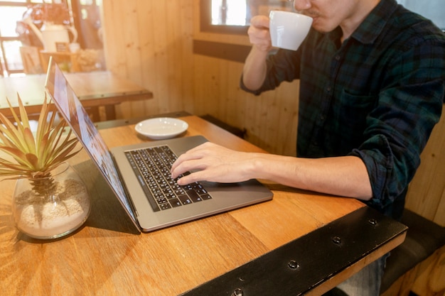 Sluit omhoog jonge mens die met zijn computer in koffiewinkel werken