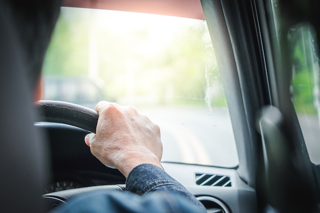 Sluit omhoog man hand drijfauto op de weg met natuurlijke achtergrond en zonlicht