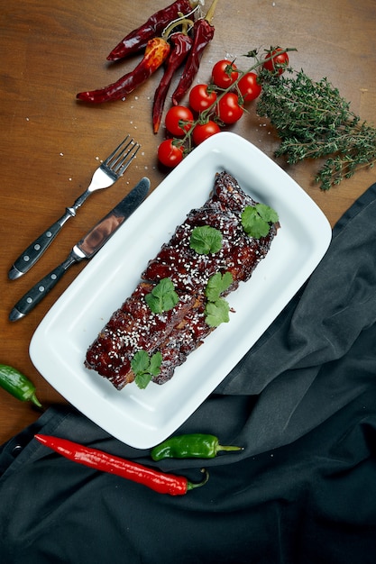 Sluit omhoog mening over smakelijke heerlijke bbq gekookte ribben met barbecuesaus in witte plaat op houten lijst. Klassiek Amerikaans geroosterd varkensvlees in samenstelling met ingrediënten