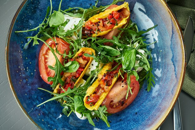 Sluit omhoog mening over Smakelijke Italiaanse caprese salade met verse tomaten, zachte mozzarella, rucola en saus in blauwe komplattelander. Bovenaanzicht, close-up