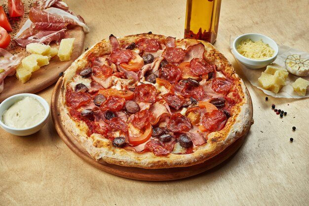 Sluit omhoog mening over Smakelijke pizza met chorizosalami, ham, gerookte worsten, tomaten en rode saus op houten lijst in een restaurant. Italiaanse keuken.