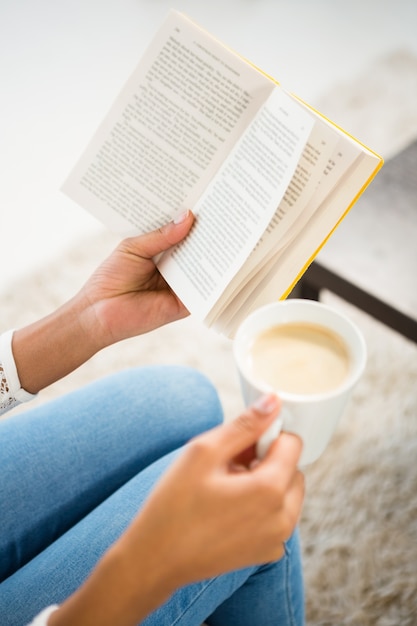 Sluit omhoog mening van de kop van de vrouwenholding van koffie en boek