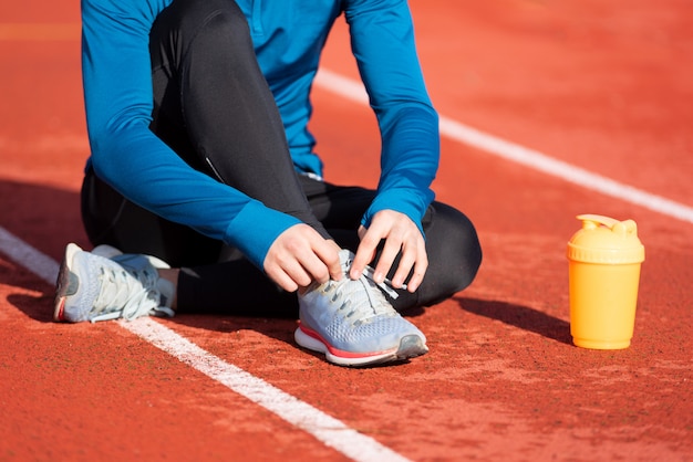 Sluit omhoog mening, van een atleet die zijn schoenkant bindt. Mens die zijn schoenkant aanhalen die op de grond op een renbaan zitten.