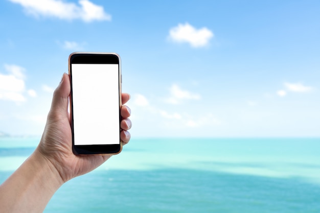 Sluit omhoog mensenhand houdend zwarte smartphone op mooie kalme blauwe overzees en witte hemelachtergrond.