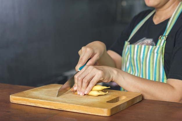 Sluit omhoog op de hand van kokvrouwen die de Groente met een mes op houten hakblok snijden