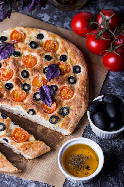 Sluit omhoog op focaccia met tomaten, zwarte olijven en basilicum