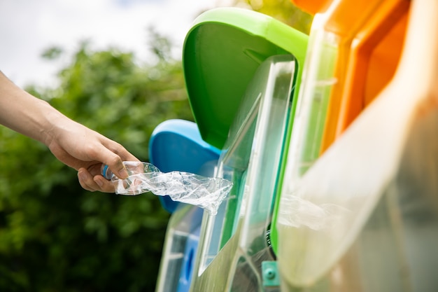 Foto sluit omhoog, overhandig het zetten van verdraaide lege plastic drinkwaterfles in kringloopbak in het openbaar.