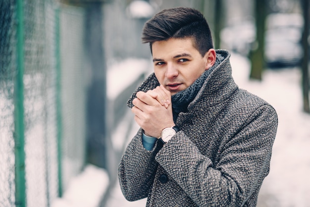 Sluit omhoog portret van de knappe jonge mens in een warme laag met modieus horloge lopend dowm de straat