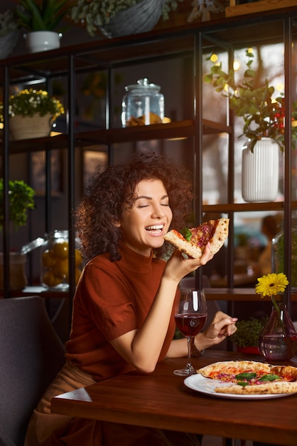 Sluit omhoog portret van een gelukkige jonge vrouw die pizza eet bij restaurant