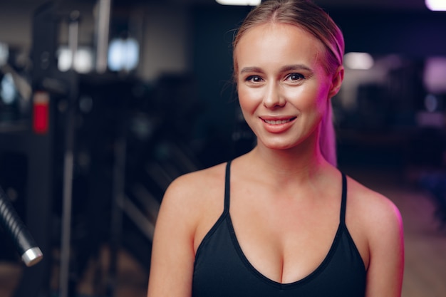 Sluit omhoog portret van een jonge blondevrouw in sportbustehouder in een donkere gymnastiek