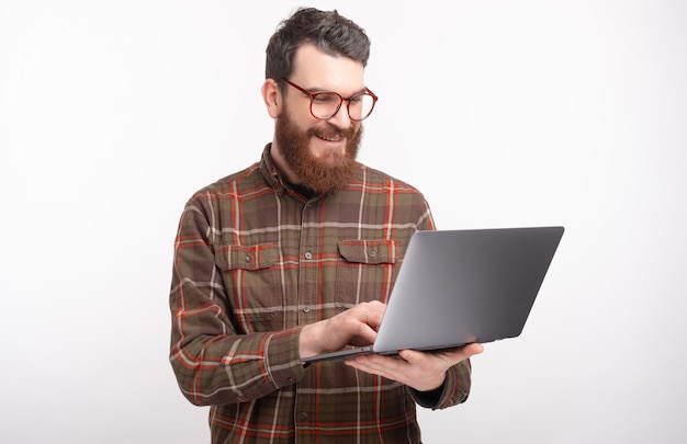 Sluit omhoog portret van een jonge gebaarde mens die en Internet op witte ruimte kijken surfen.