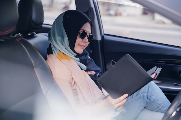Sluit omhoog portret van een jonge moslim bedrijfsvrouwenlezing in de achterbank van de auto.