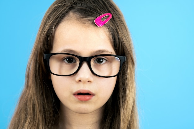 Sluit omhoog portret van een kindschoolmeisje die kijkend die glazen dragen op blauwe achtergrond wordt geïsoleerd