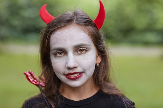 Foto sluit omhoog portret van glimlachende tienermeisje die duivelskostuum en schmink in openlucht dragen