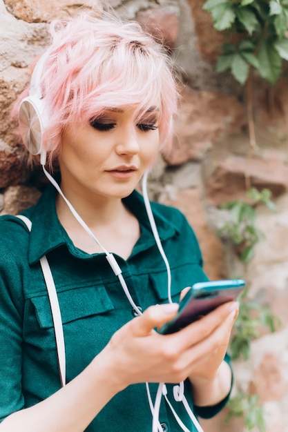 Sluit omhoog portret van jonge vrouw freelancer die met roze kapsel aan muziek op oortelefoons luistert