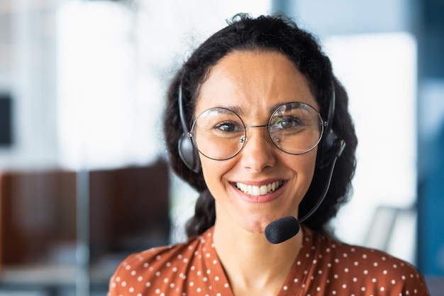 Sluit omhoog portret van Latijns-Amerikaanse vrouw binnen modern bureau met hoofdtelefoon voor videovraagvrouw