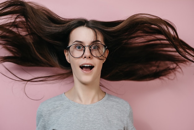 Sluit omhoog portret van verraste vrouw in glazen met vliegend haar en wijd open mond.