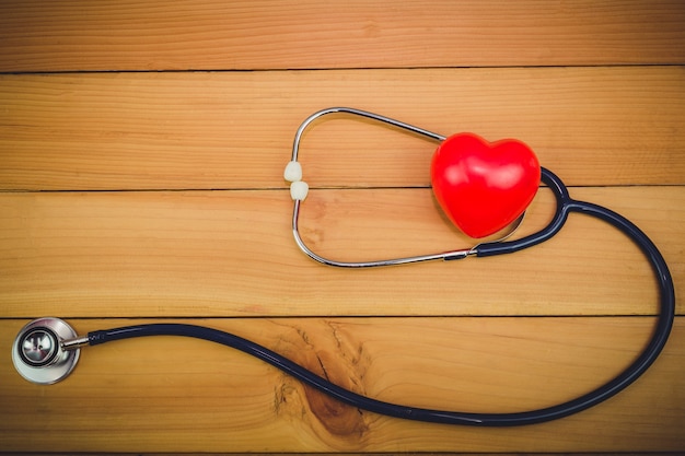 Foto sluit omhoog rood hart en steythoscope op oude houten lijst