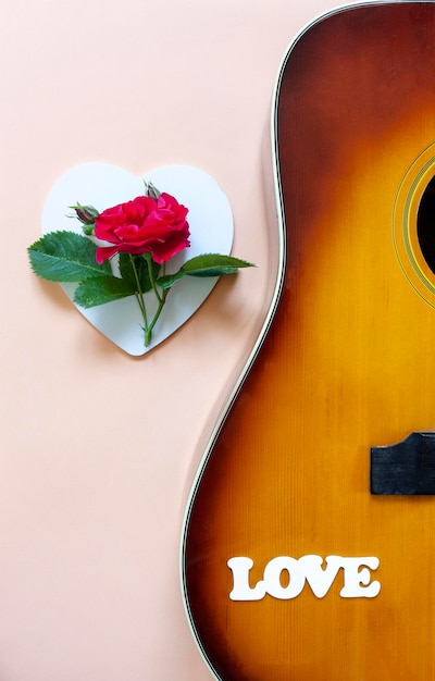 Foto sluit omhoog van akoestische gitaar met mooie tot bloei komende roze bloem en woordliefde