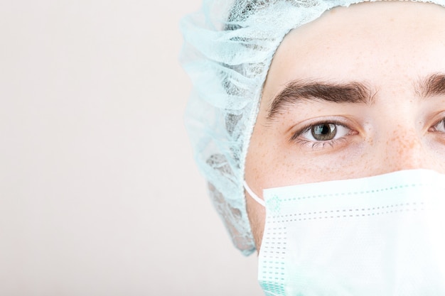 Sluit omhoog van Amerikaanse mannelijke arts of chirurg in beschermend gezichtsmasker over grijs
