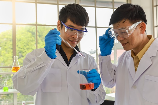 Sluit omhoog van aziatische professionele hogere artsenwetenschapper onderwijzen en begeleiden aziatische jonge wetenschapper gebruikend pipet om te testen en onderzoek naar werkend laboratorium.
