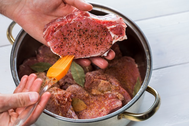 Sluit omhoog van chef-kokshanden die het vlees kruiden. Braadpan met rauw vlees op een witte achtergrond.