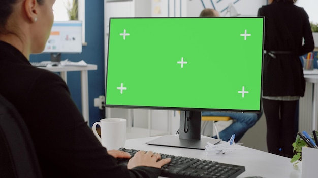 Sluit omhoog van computer met horizontaal groen scherm op bureau. Vrouw met zakelijke baan bezig met monitor met mockup sjabloon en geïsoleerde achtergrond voor technologie met Chromakey.
