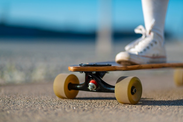 Sluit omhoog van damebeen in witte tennisschoenen die na extreme grappige rit rusten haar houten longboardskateboard. Moderne stedelijke hipster meisje veel plezier. Goede zonnige zomerdag om te skateboarden en plezier te hebben