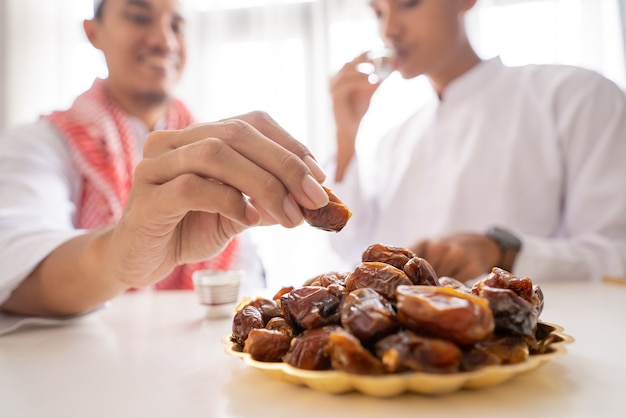 Sluit omhoog van de hand van de moslim die dadels neemt terwijl hij thuis geniet van een iftar-diner tijdens een ramadan-feest