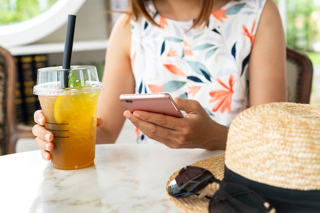 Sluit omhoog van de handen die van vrouwen dranken houden terwijl het gebruiken van mobiele telefoon in koffie.