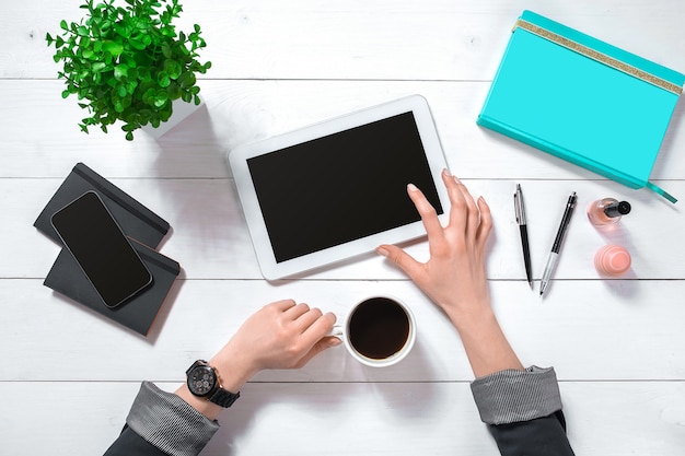 Sluit omhoog van de handen van de vrouw met lange vingers die tablet houden. Smartphone en notebook liggen op tafel. Bovenaanzicht. Ruimte kopiëren