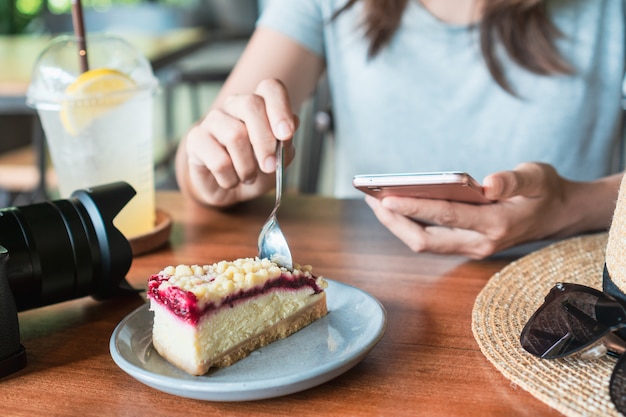 Sluit omhoog van de handen van vrouwen houdend mobiele telefoon terwijl het eten van cake in koffie.