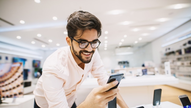 Sluit omhoog van de knappe jonge mens die nieuwe mobiel in de elektronische winkel kopen.