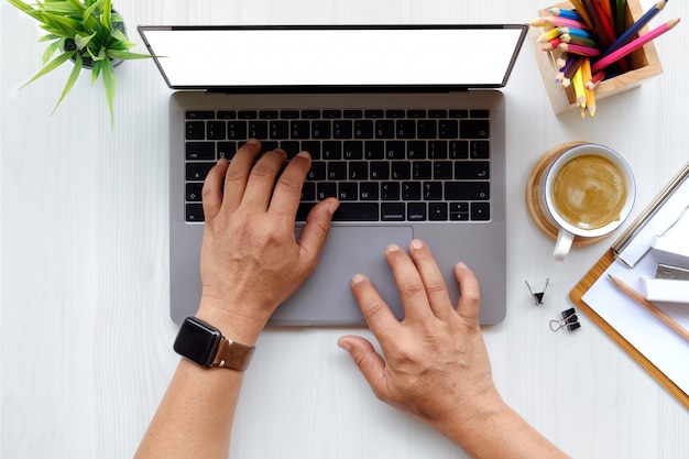 Sluit omhoog van de mens die aan laptop werken terwijl het zitten bij het witte houten bureau in modern bureau.