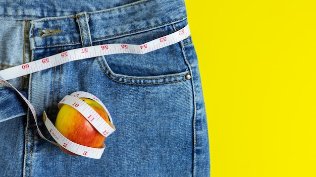 Sluit omhoog van de rode appel op jeans die rond een meetlint, een gezondheid en op dieet zijn concept wordt verpakt