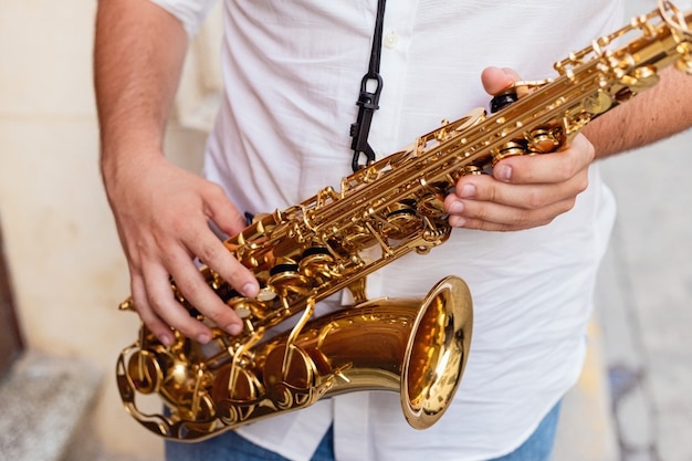 Sluit omhoog van een mens die zijn saxofoon op de straat houdt