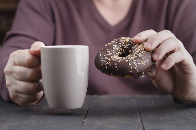 Sluit omhoog van een mensenholding in zijn handen een doughnut met chocolade