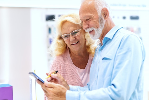 Sluit omhoog van glimlachend oud paar die tablet uitproberen terwijl status in technologie-opslag.