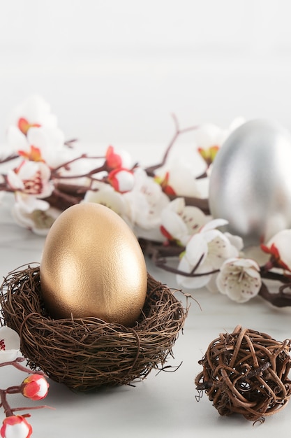 Sluit omhoog van gouden en zilveren paaseieren in het nest met witte pruimbloem op heldere witte houten lijstachtergrond.