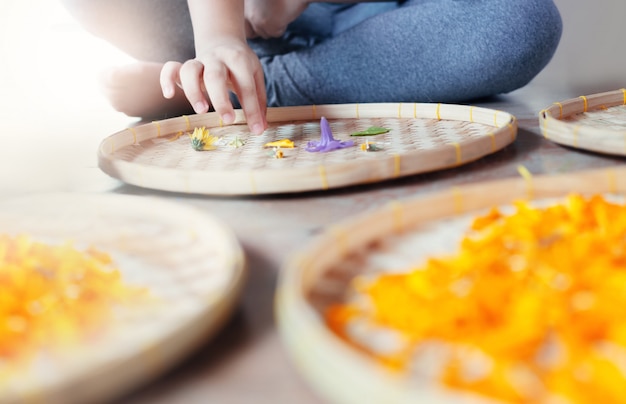 Sluit omhoog van hand van jonge meisjesbloemist die bloemmandala op rieten mand creëren.