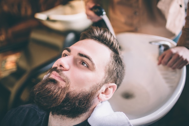 Sluit omhoog van het hoofd van de klant dat door haarstylist wordt gewassen. Hij wast het met water. De procedure is zachtaardig en vol zorg.