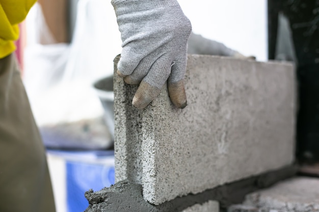 Sluit omhoog van industriële metselaar die bakstenen installeren op bouwwerf, die muren bouwen.